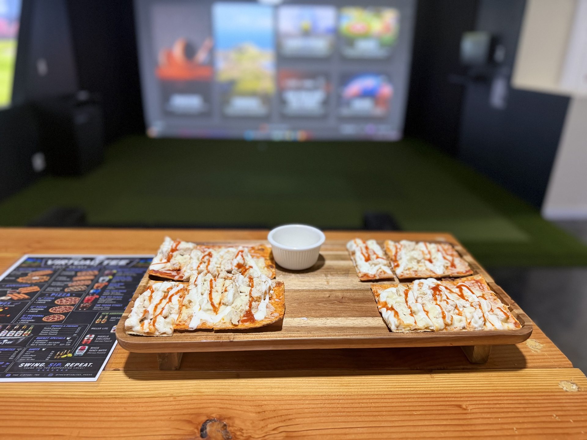 Flatbreads on a wooden serving board in front of a simulator bay screen at The Virtual Tee